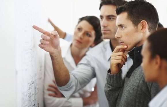 Group of business associates looking and pointing at a chart put up on the wall